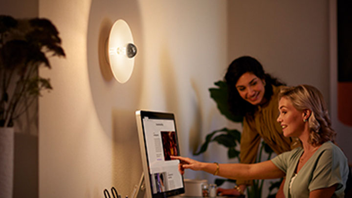 Donne al computer accanto a una lampada LED specchio montata a parete