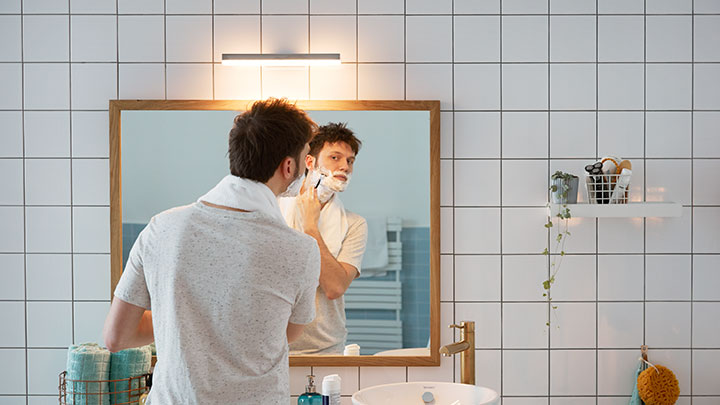 Uomo che si rade davanti allo specchio del bagno illuminato da un LED Philips montato a parete
