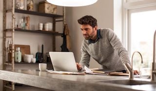 Uomo che usa il computer portatile in un ufficio domestico ben illuminato con lampada da scrivania LED per una configurazione efficiente per il lavoro da remoto.