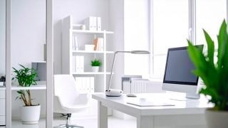 Una stanza bianca e luminosa mostra una scrivania con un computer e una lampada da tavolo su di essa