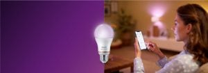 Donna che controlla l'illuminazione a LED intelligente tramite app per smartphone, creando un'atmosfera calda in un accogliente soggiorno grazie alla tecnologia domestica connessa.