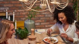 Cucina moderna con lampadari a LED in stile vintage che illuminano due donne che cenano, creando un'atmosfera calda e invitante.