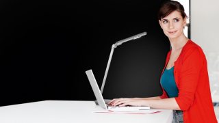 Donna che studia alla scrivania con una lampada LED regolabile, che fornisce un'illuminazione ottimale per i compiti in uno spazio colorato per l'apprendimento a casa.